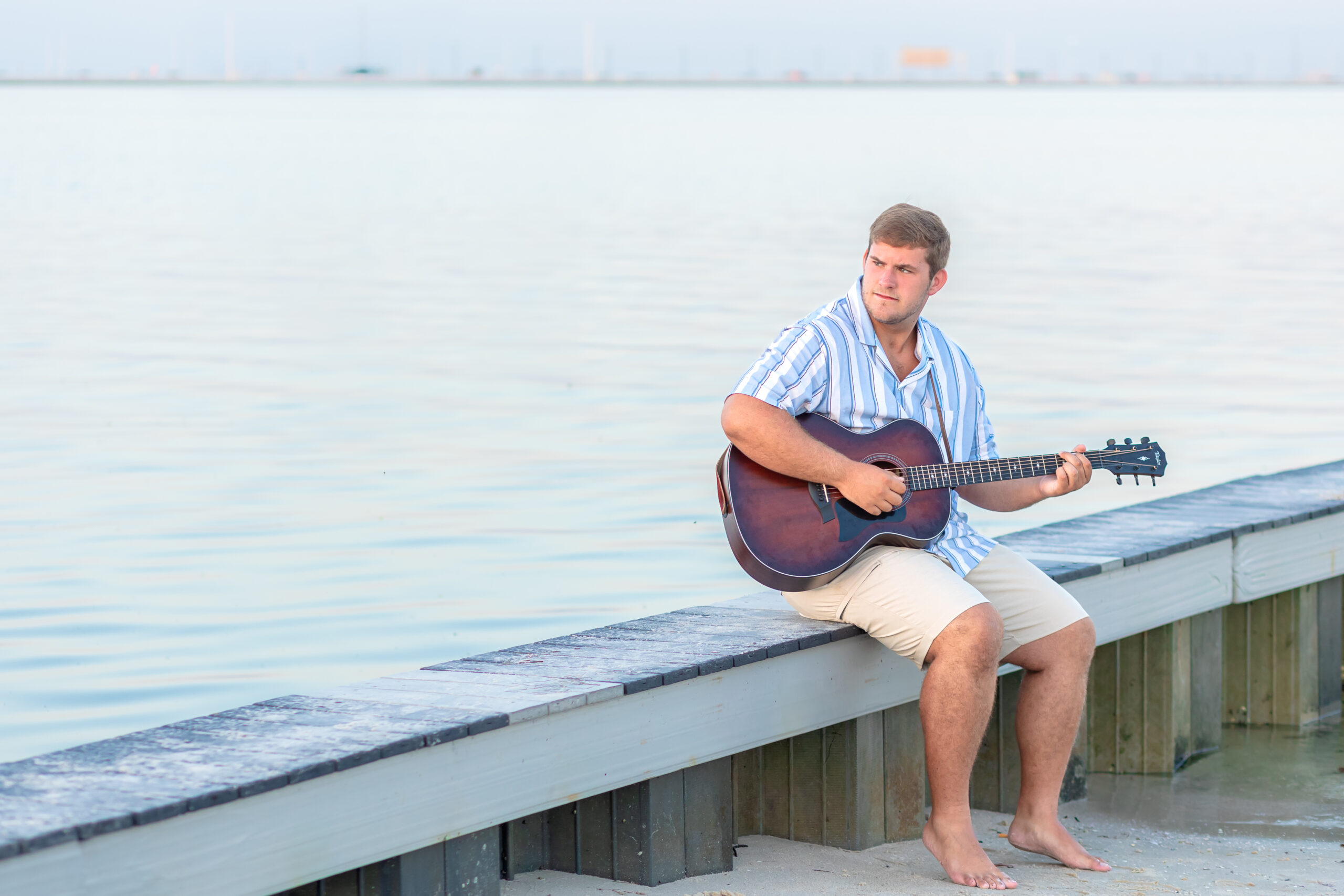 A senior guy sitting on a dock with his guitar, at sunrise.